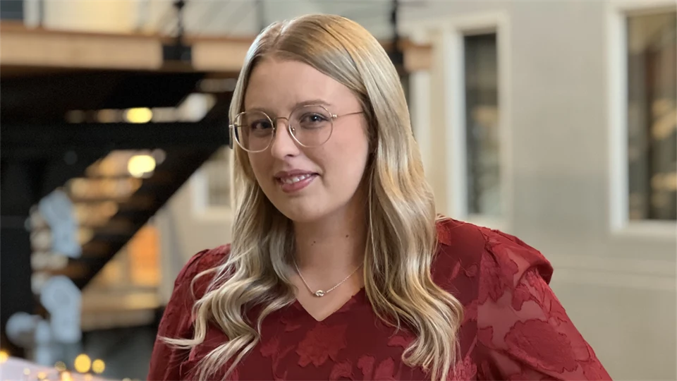 En ung kvinna med långt hår och glasögon tittar in i kameran.