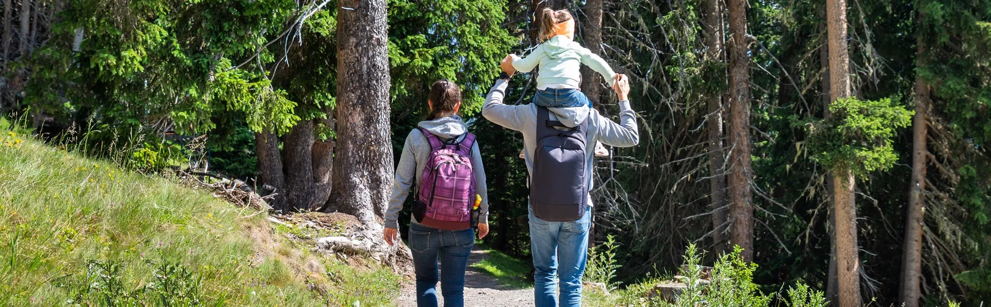kvinna med ryggsäck  och man med barn på axlarna vandrar i skogen
