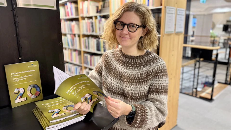 Person som står och bläddrar i den gröna jubileumsboken.