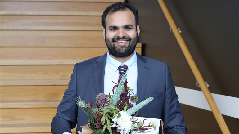Porträtt på doktor Waqas Ahmad som håller blommor och avhandling i handen