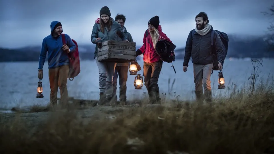 Five people walk with lanterns by the beach at he High Coast in Sweden