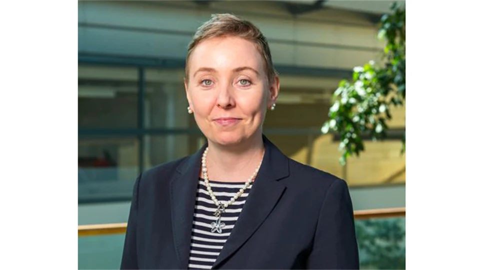 A woman with light, short hair, wearing a striped sweater and blue jacket.