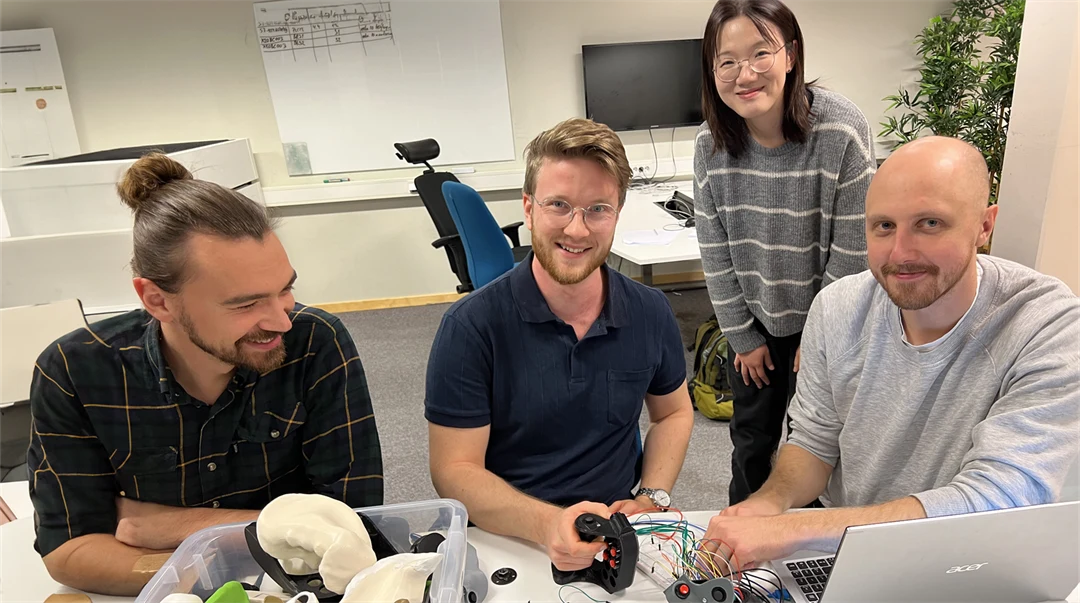 Några personer är tillsammans vid ett bord med elektronik och andra saker i en plastlåda.