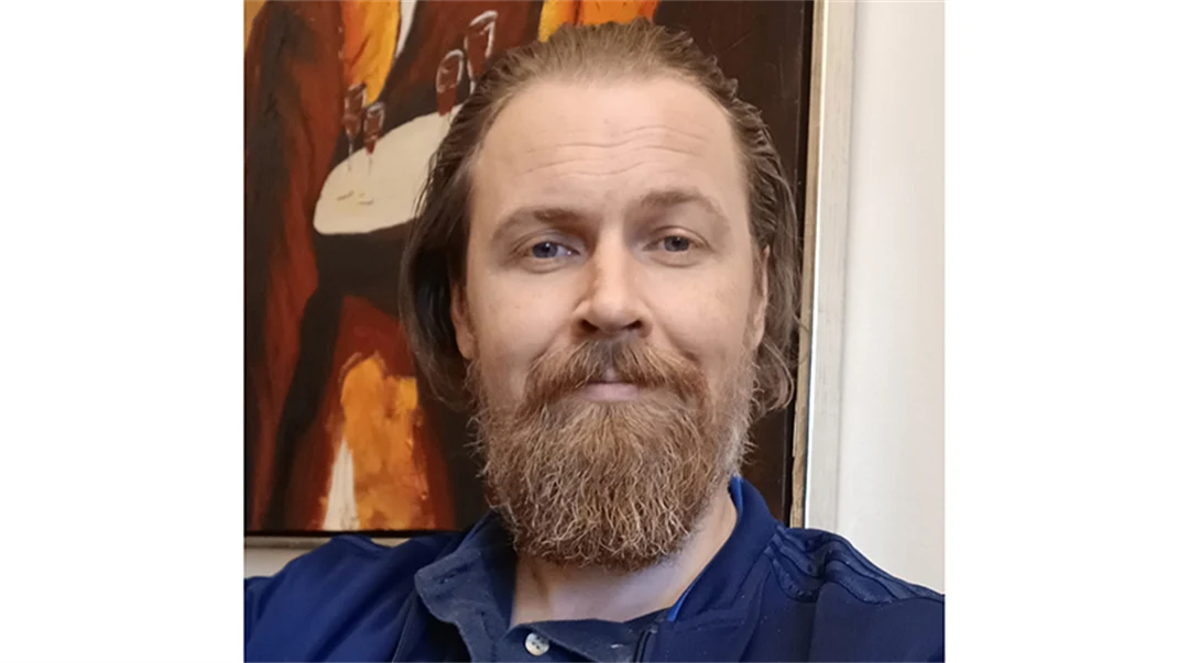 Man med rödlätt hår och skägg, klädd i en blå skjorta.