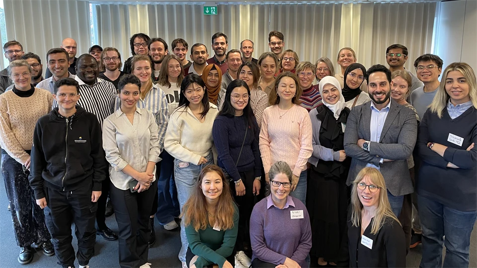 En stor grupp personer står tillsammans i ett rum och tittar in i kameran.