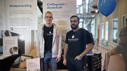 Två personer står bakom ett bord framför roll-ups med programbeskrivning för civilingenjörsprogrammet i datateknik.