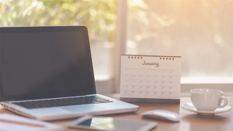 Ett bord med en laptop, kalender och kaffekopp