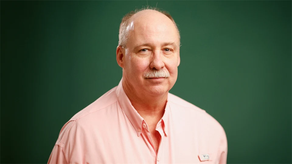  A man in a pink shirt looks into the camera.