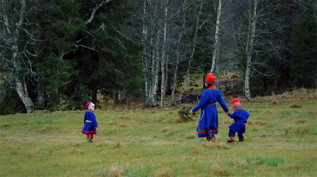 Kvinna och två barn i sydsamiska dräkter går över ett fält.