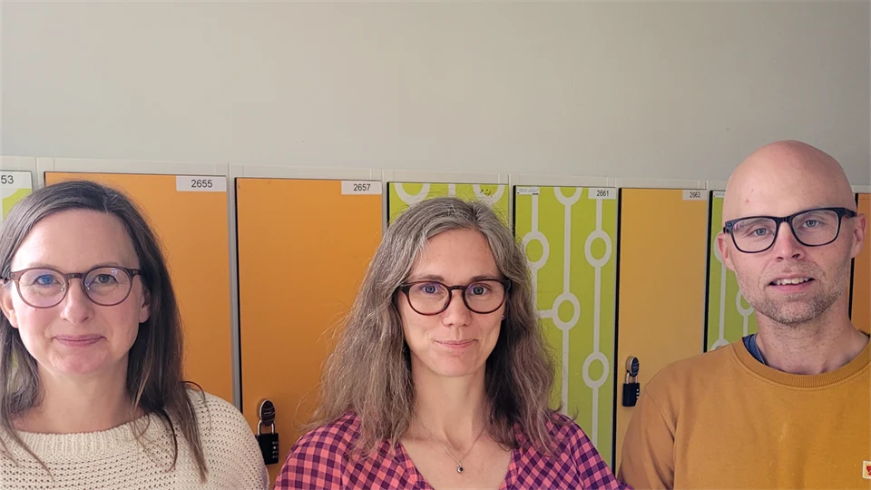 Två kvinnor och en man står framför gula skåp i en skola