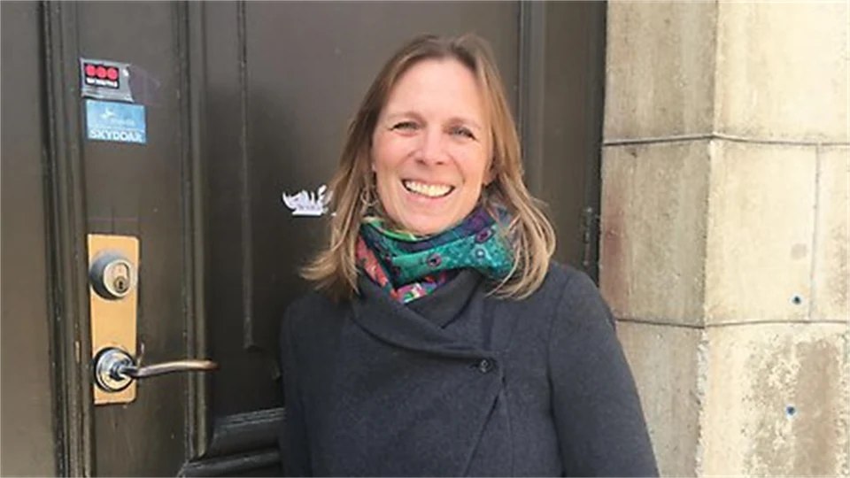 Woman in gray jacket and colorful scarf in front of a brown door