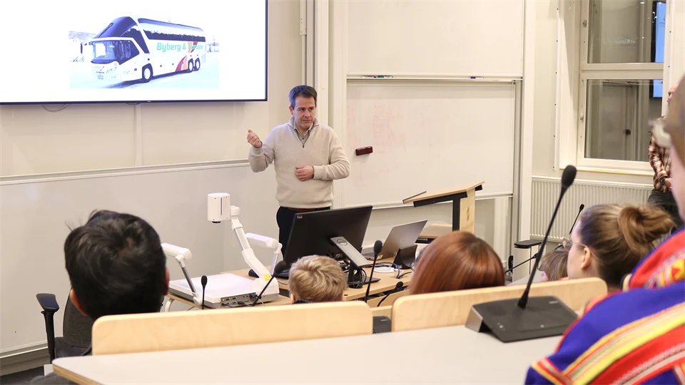En man i ljus tröja står och presenterar för en publik