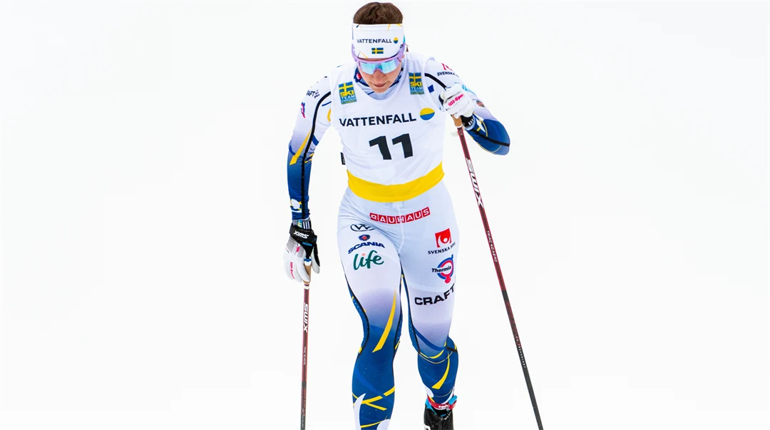 Kvinnlig längdskidåkare mot vit bakgrund.