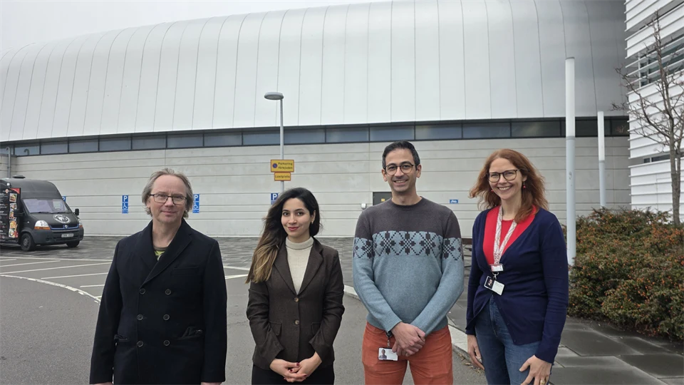 Four people, two men and two women, are standing outside in front of a large building. 