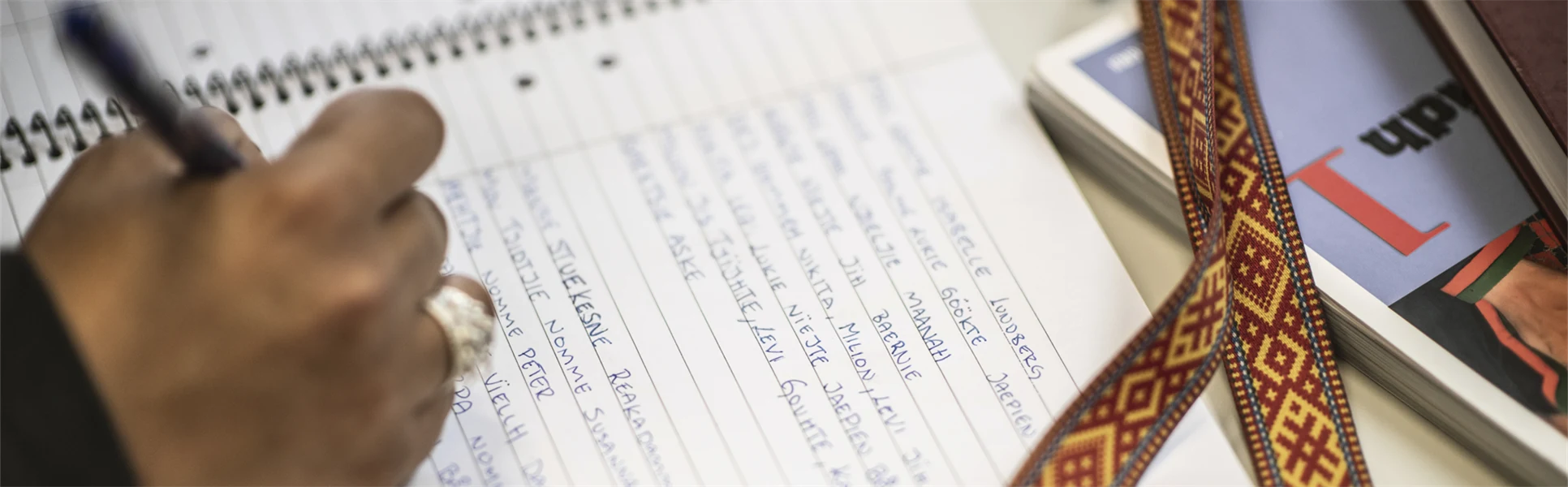 Hand som skriver i ett block intill ett samiskt band